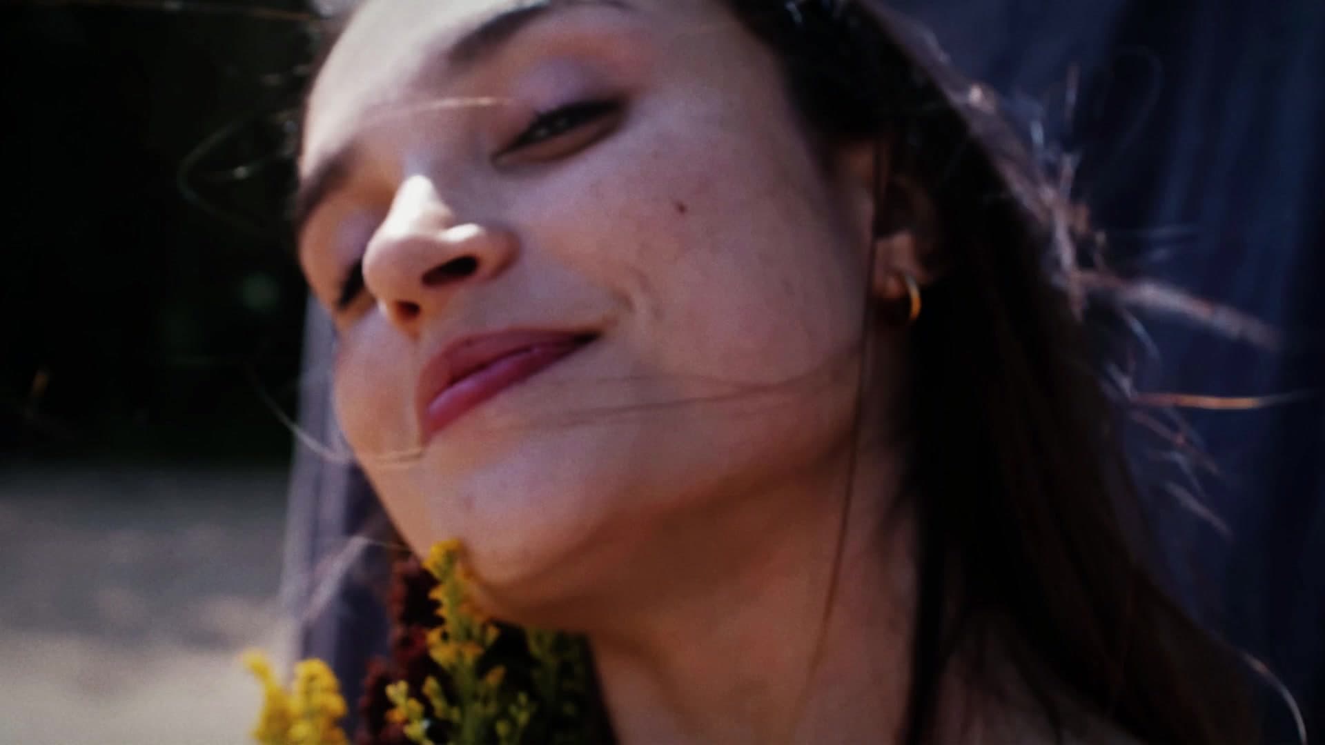 A woman smiling with her eyes closed, holding yellow flowers