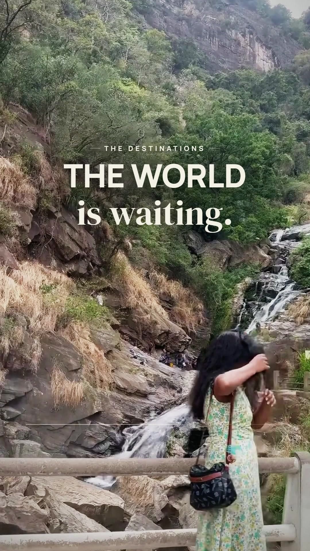 A traveller at a waterfall viewpoint under the words THE WORLD is waiting